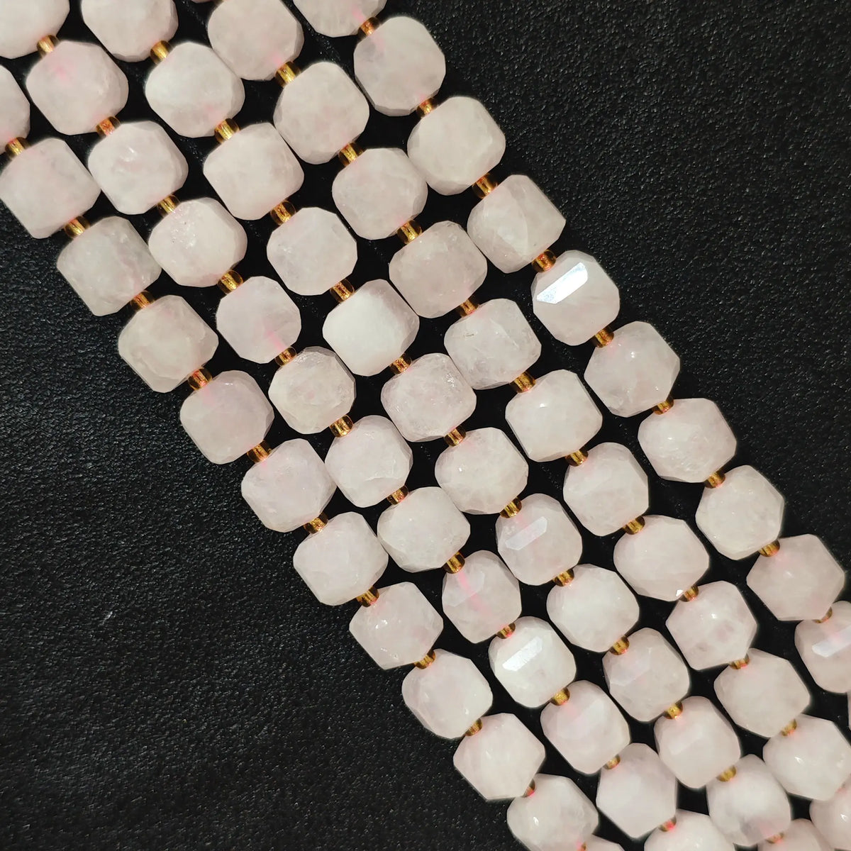 Multiple parallel strands of natural rose quartz 10mm soft-tumbled cube beads viewed from distance showing soft pink tones