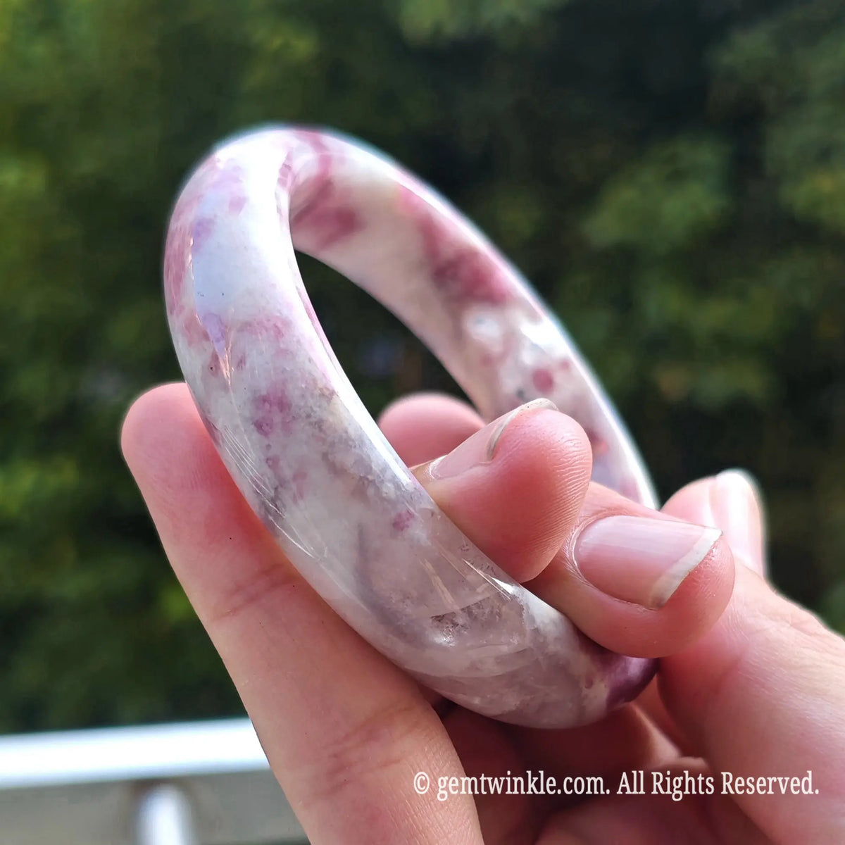 Hand holding plum blossom tourmaline bangle under natural sunlight revealing vibrant pink mineral distribution