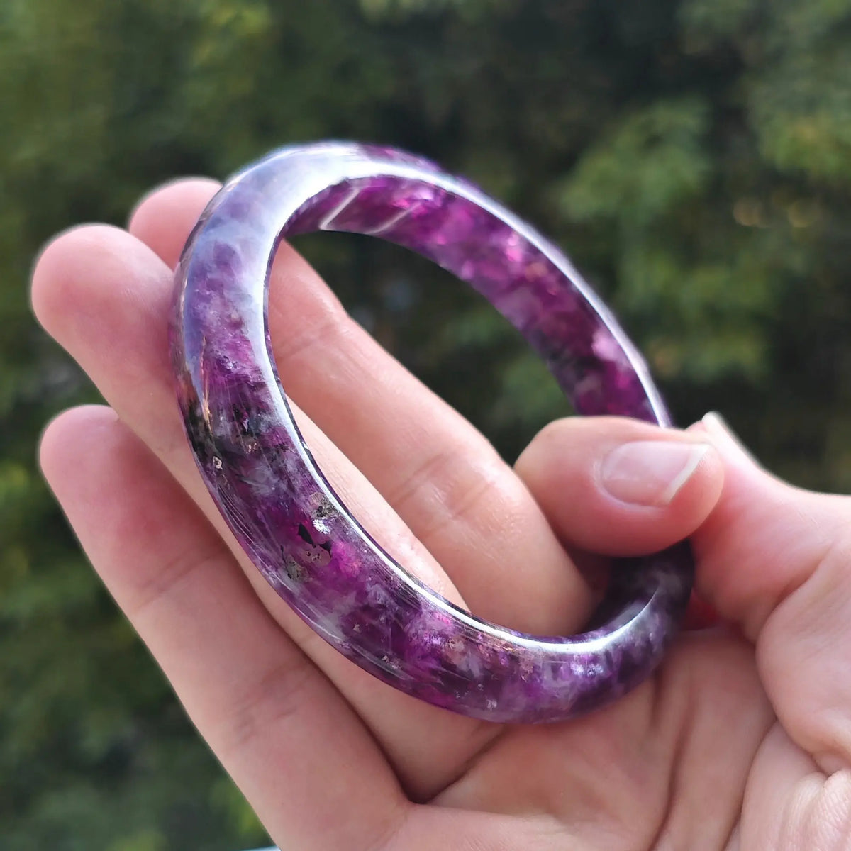 Natural purple lepidolite bangle held in hand showing rich violet color and glossy polished surface