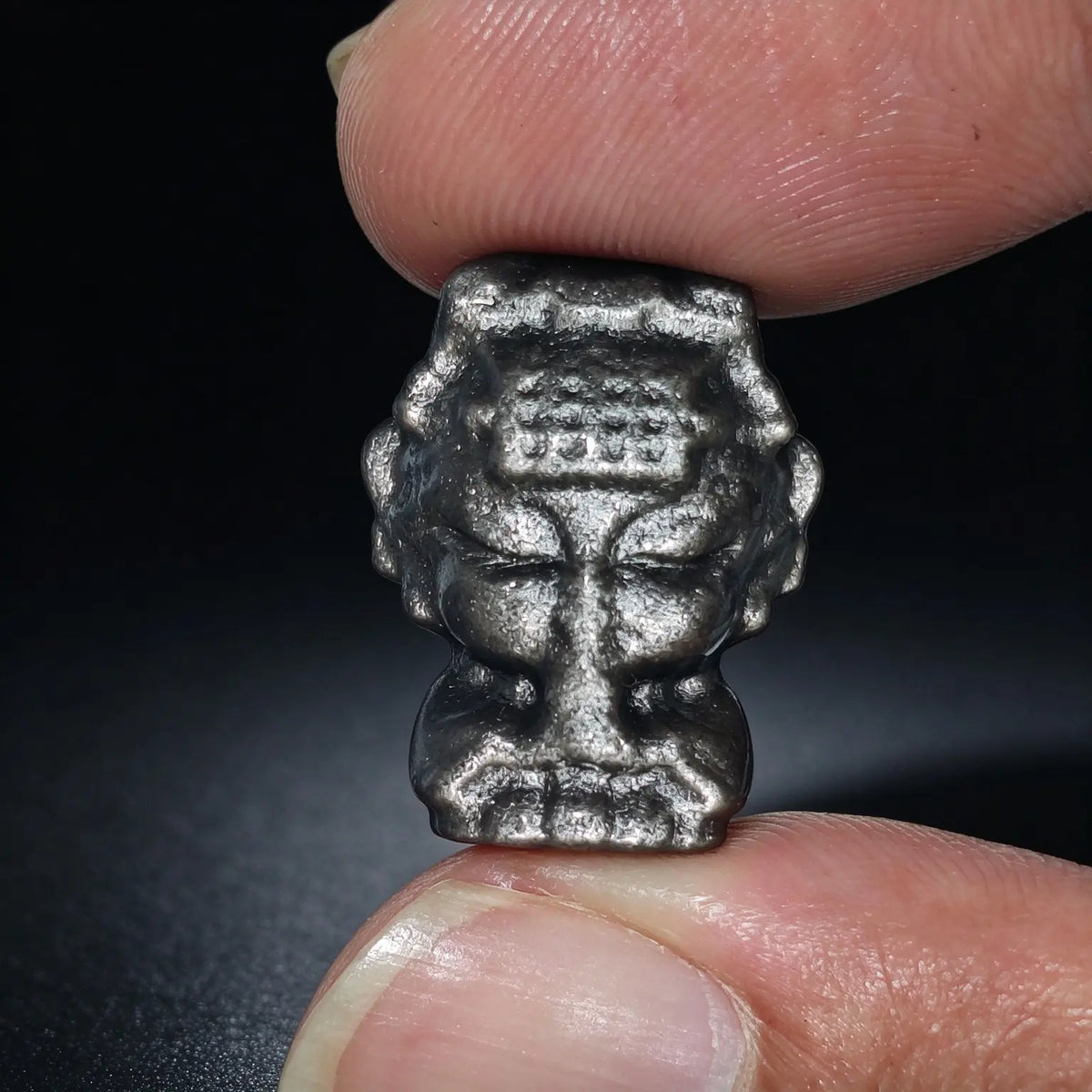 Fingers holding a natural silver sheen obsidian Mazu goddess carved focal bead showing metallic silver reflection under light