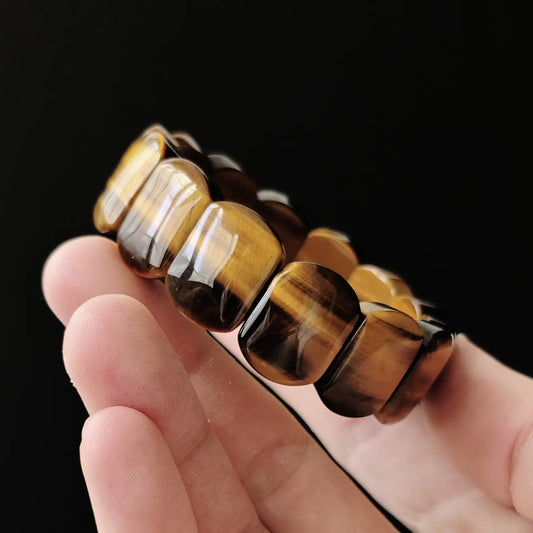 Genuine natural tiger’s eye oval beads (~19mm length), golden-brown bands with silk-like chatoyancy, stretch elastic—held in hand on black background