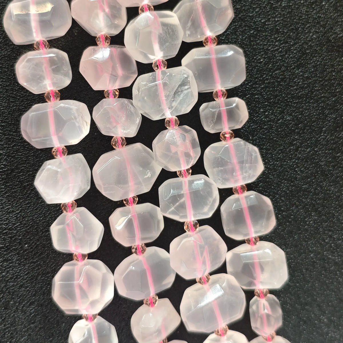 Strands of natural translucent rose quartz faceted freeform beads displaying soft pink ice-crystal luster on dark background