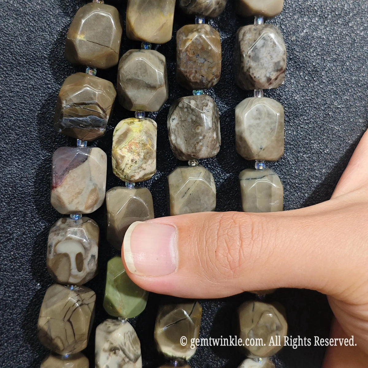 Strands of natural volcanic ash agate freeform beads aligned on dark background showing earth tone variations