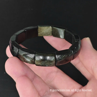Gold sheen obsidian bangle style plate stretch bracelet resting on palm displaying metallic gold sheen reflection