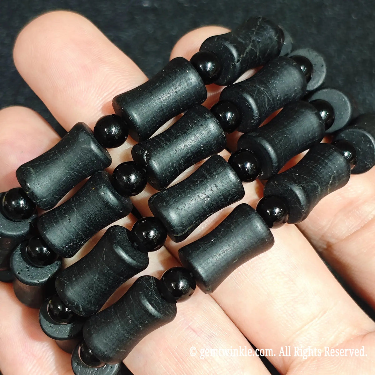 Hand holding three natural matte black tourmaline barrel stretch bracelets showing rustic matte finish and parallel growth lines