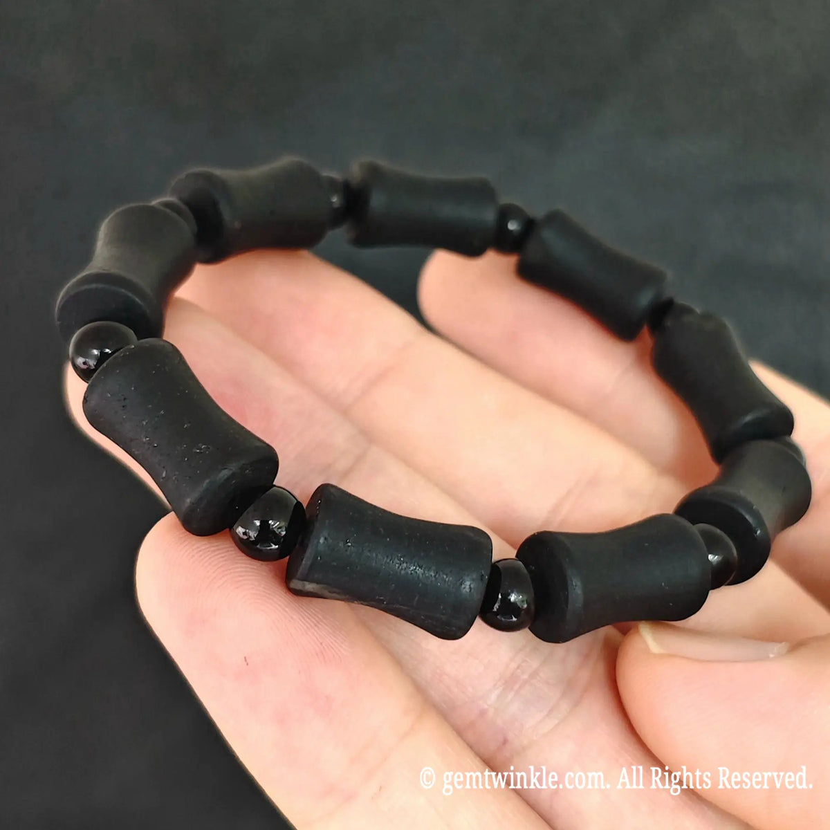 Close up view of natural matte black tourmaline barrel beads showing parallel surface growth grooves and polished spacer beads