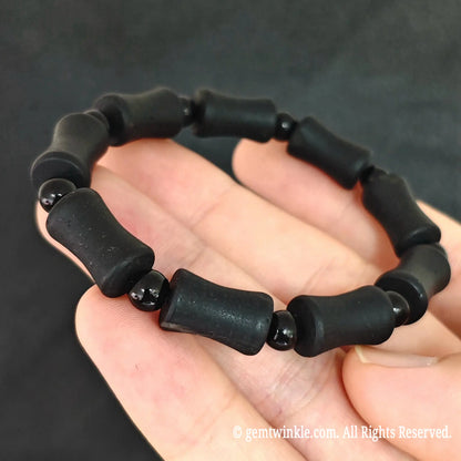 Close up view of natural matte black tourmaline barrel beads showing parallel surface growth grooves and polished spacer beads