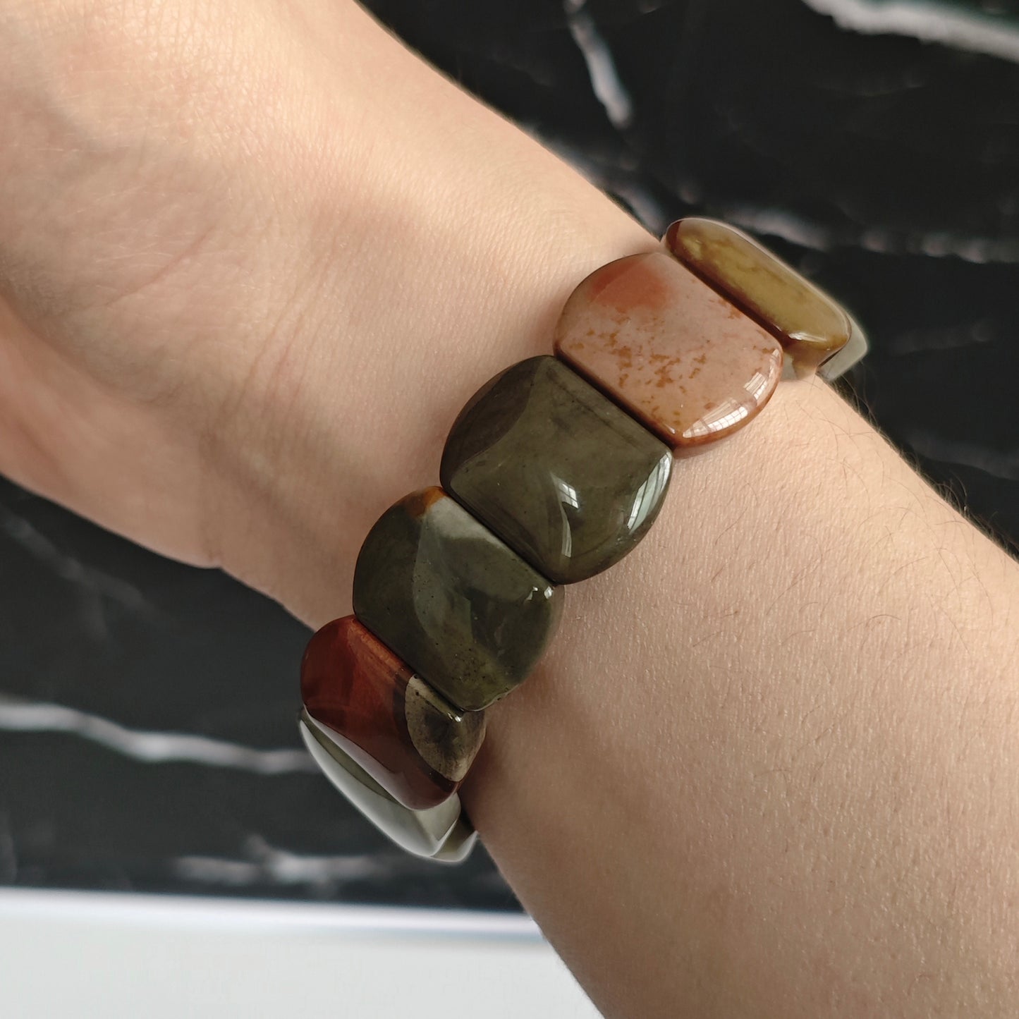 Ocean jasper multi-color bracelet worn on wrist; organic patterns and earthy tones visible under soft lighting
