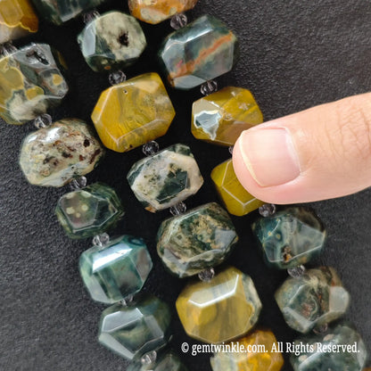 Hand holding three strands of natural ocean jasper faceted chunky beads showing multi color volcanic matrix
