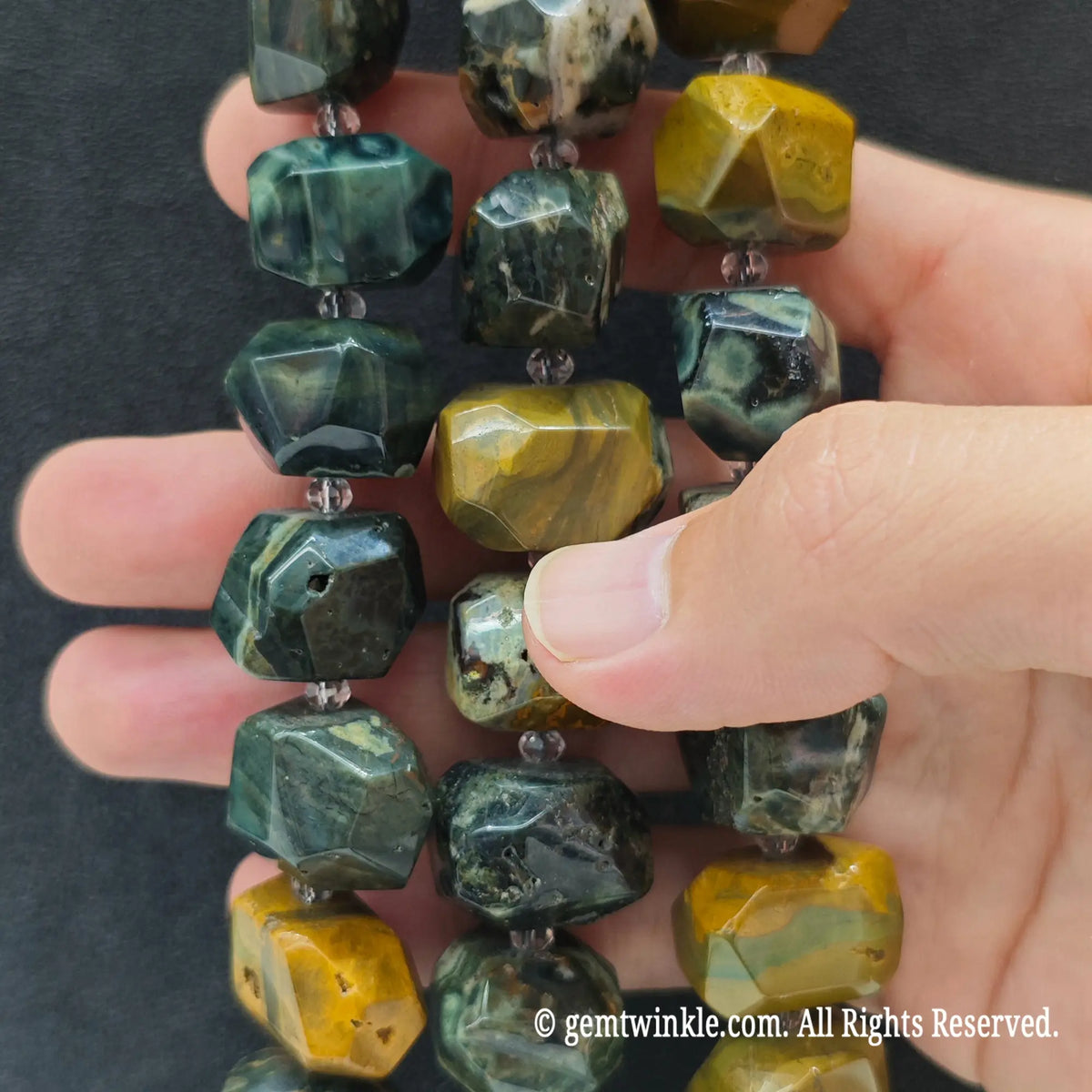 Finger pointing to a large natural ocean jasper faceted chunky bead displaying organic mineral cavities and yellow matrix