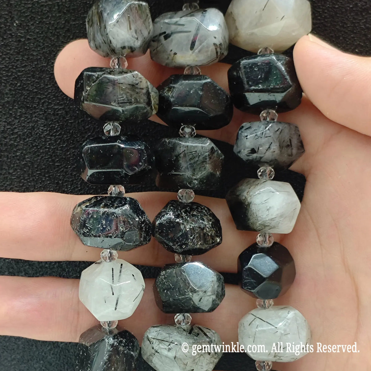 Hand holding three strands of natural milky black rutilated quartz faceted beads showing opaque white quartz matrix