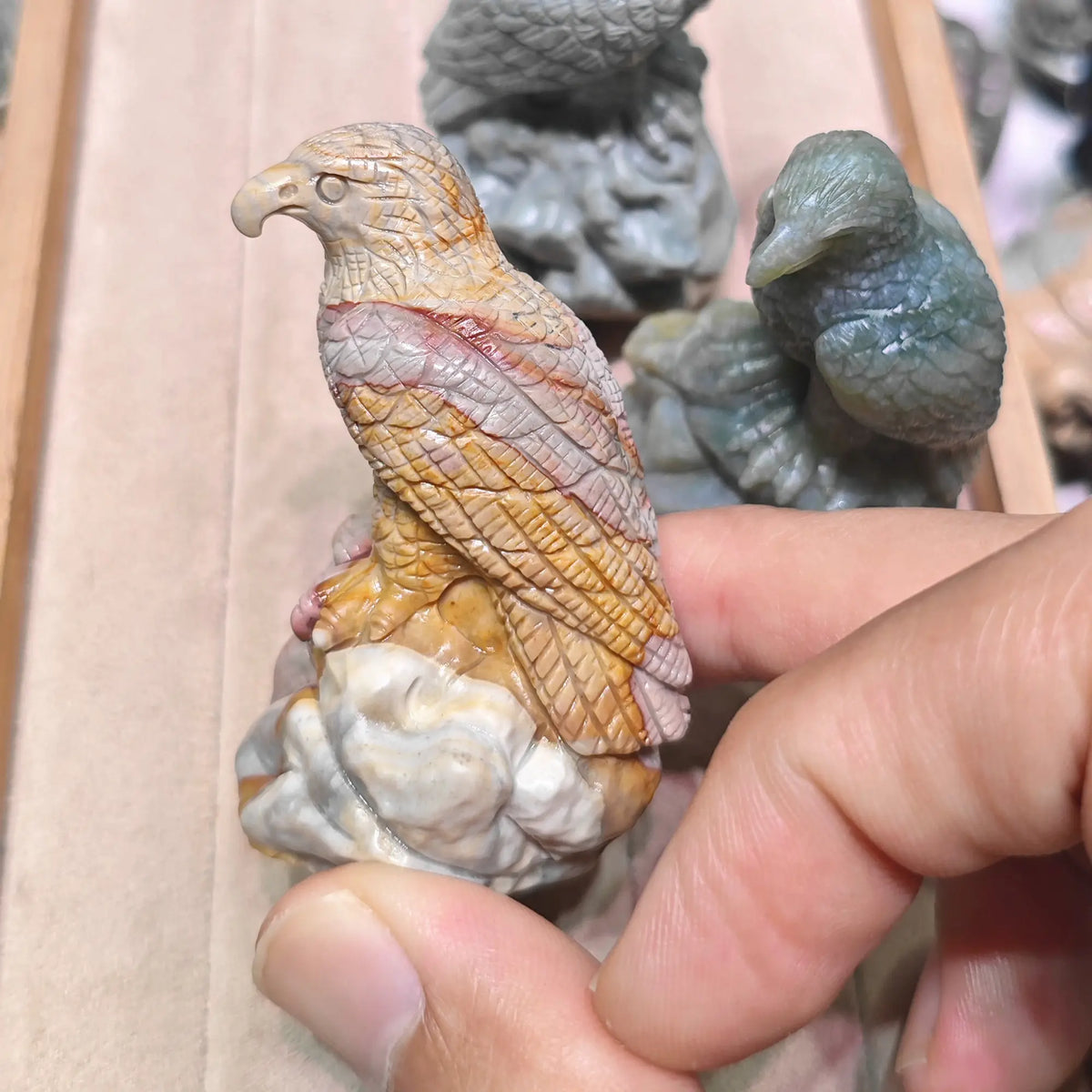 Close up perspective of the carved wing patterns and stone base on a golden red eagle statue held gently by a hand