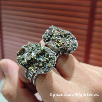 Hand holding two oversized natural pyrite calcite druzy cocktail rings mounted on textured silver tone alloy bands
