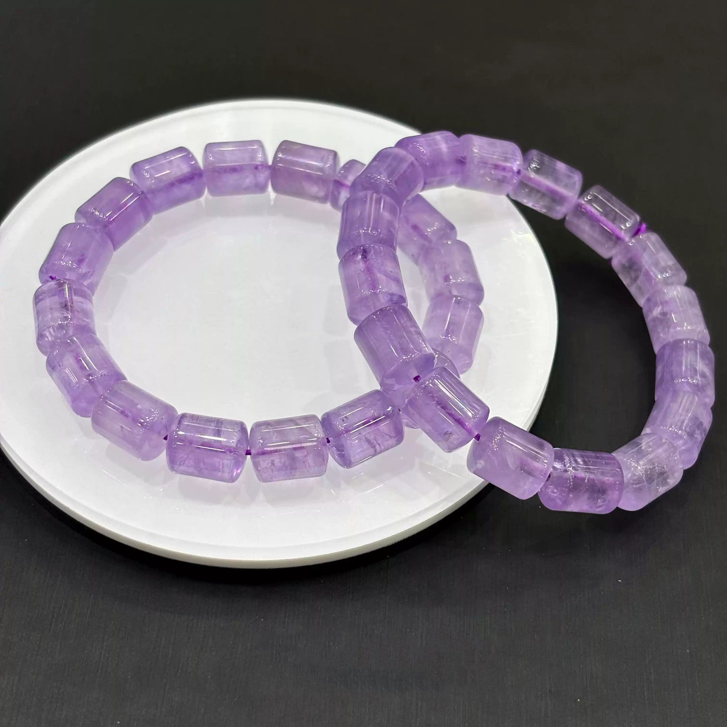 Two light purple amethyst crystal bracelets placed side by side on a white dish over dark surface, emphasizing symmetry, clarity, and natural stone texture.