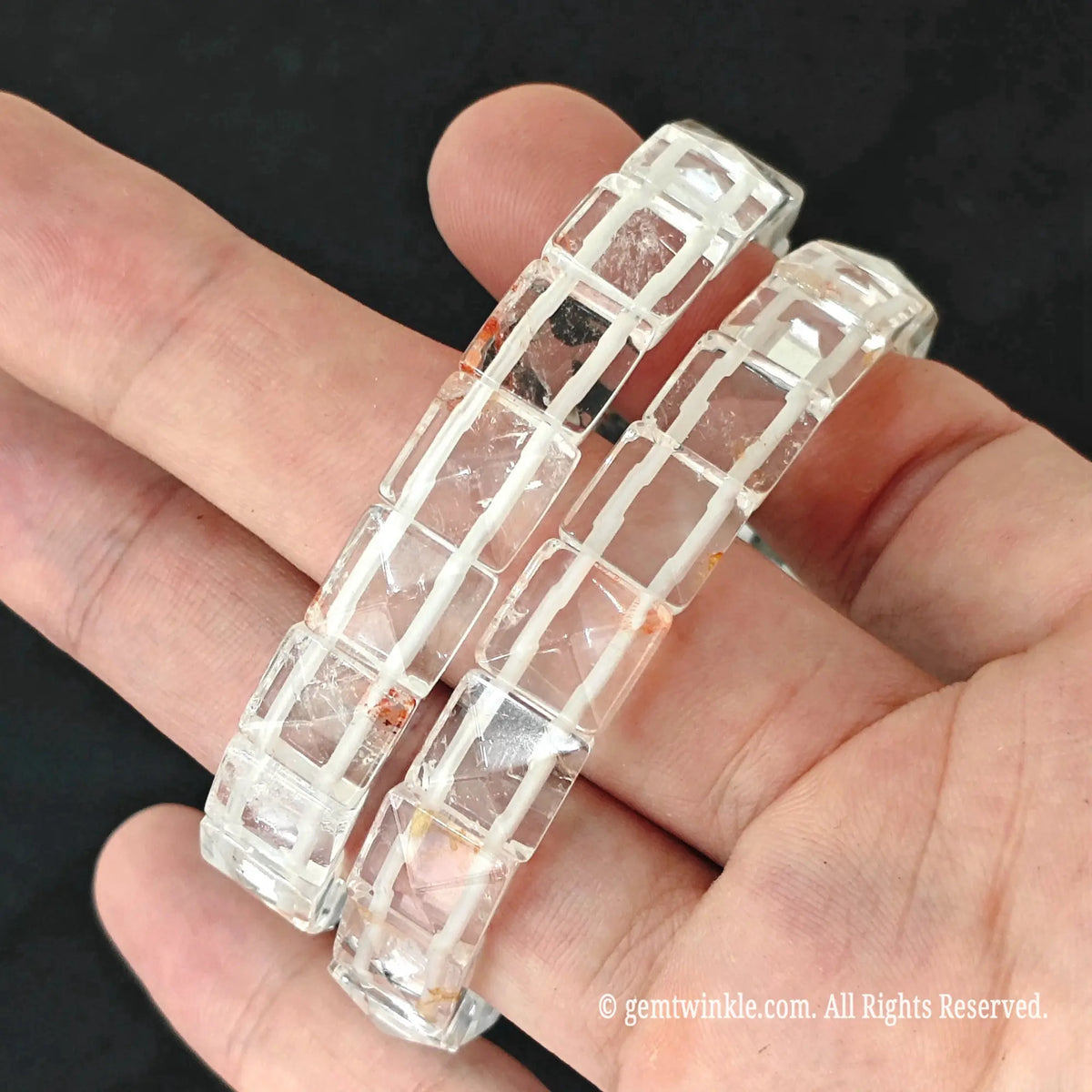 Hand holding two clear quartz pyramid tile stretch bracelets showing smooth polished geometric facets