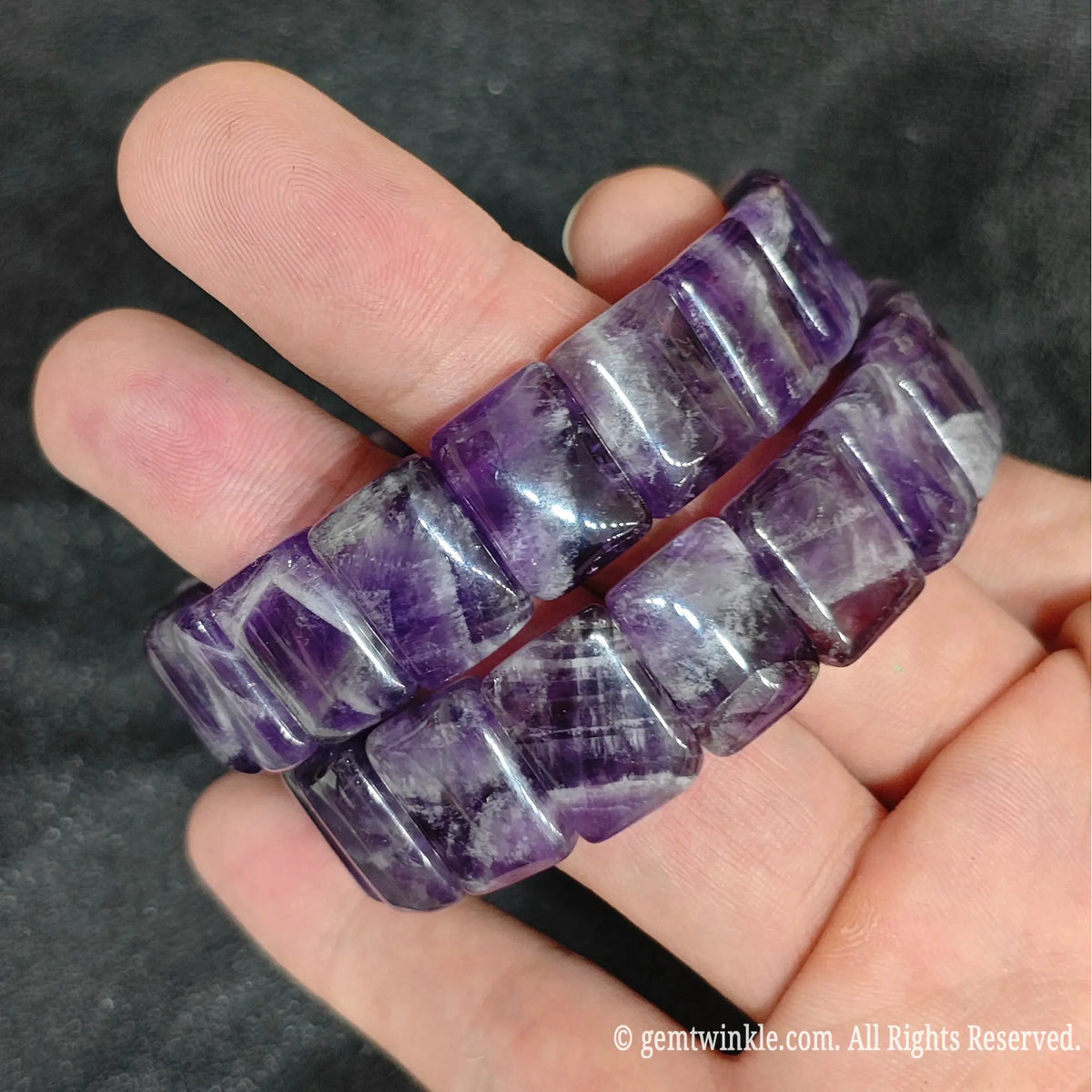 Hand holding two dark velvet chevron amethyst smooth block stretch bracelets showing polished curved surfaces