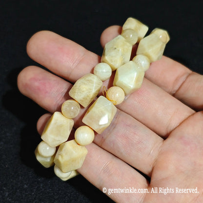Hand holding two natural golden yellow quartzite faceted stretch bracelets showing alternating round spacer beads