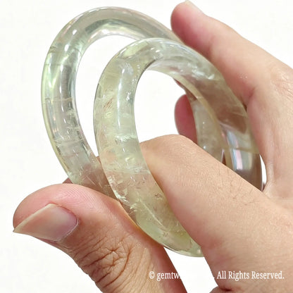 Close up view of two solid lemon quartz crystal bangles held between fingers displaying high gloss finish