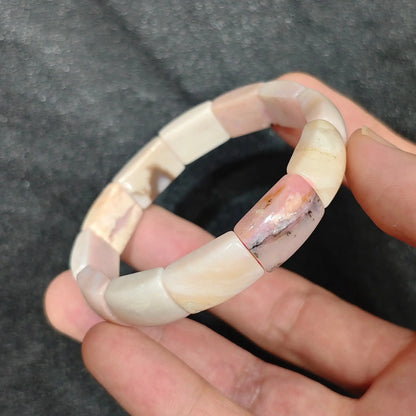 Natural pastel pink opal smooth curved segment stretch bracelet held on hand displaying soft blush pink tones and porcelain sheen