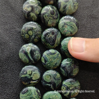 Hand showing flat round coin peacock eye stone loose beads highlighting forest green orbicular eye markings