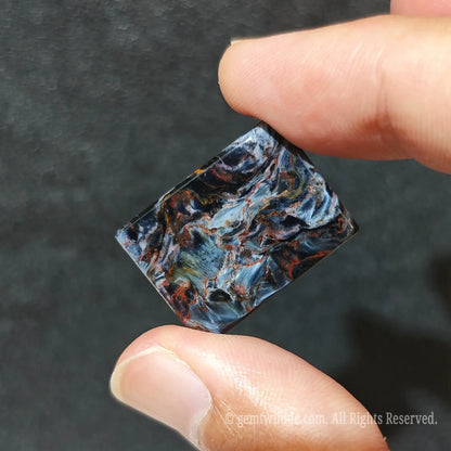 Close up view of rectangular petersite cabochon resting on palm highlighting silky fiber reflections
