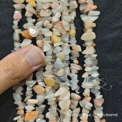 Close up hand holding natural pink aventurine stone chips displaying polished surfaces and fine drill holes