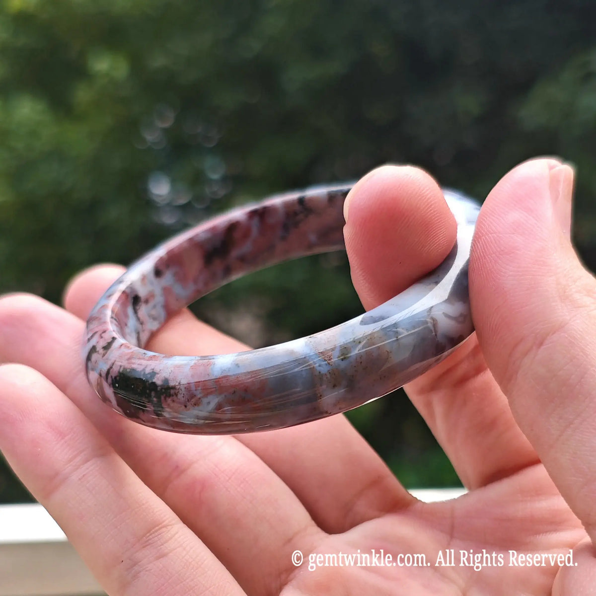Close up view of natural pink ocean jasper bangle highlighting ice blue and dark red orbicular jasper eyes