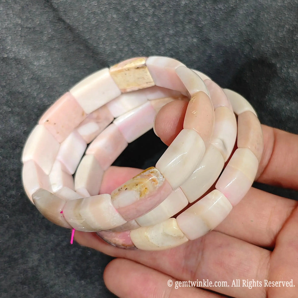 Side view of three natural pastel pink opal curved segment stretch bracelets showing double row elastic construction and smooth texture