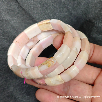 Side view of three natural pastel pink opal curved segment stretch bracelets showing double row elastic construction and smooth texture