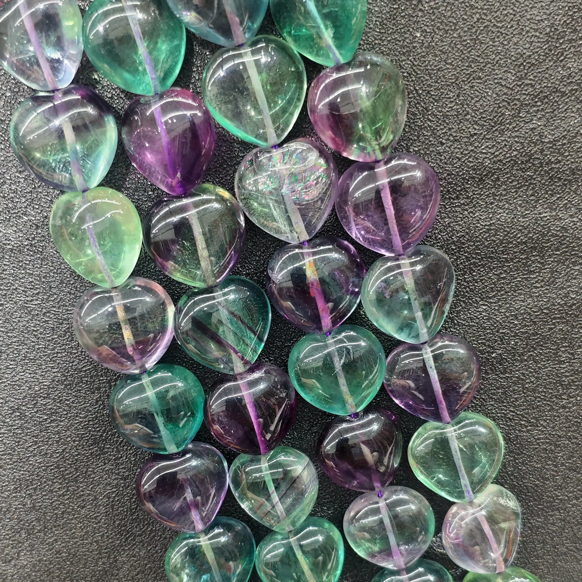 Strands of high clarity rainbow fluorite heart beads displaying purple green and blue transparent crystal color banding