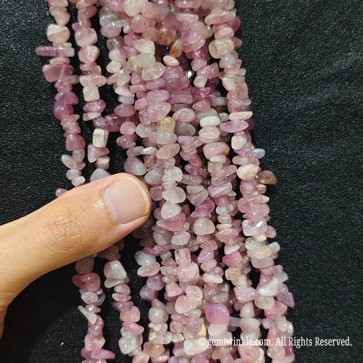 Close up hand holding natural lavender pink stone chips displaying polished surfaces and fine drill holes