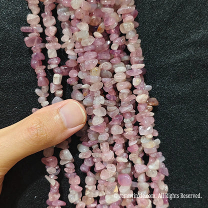 Close up hand holding natural lavender pink stone chips displaying polished surfaces and fine drill holes
