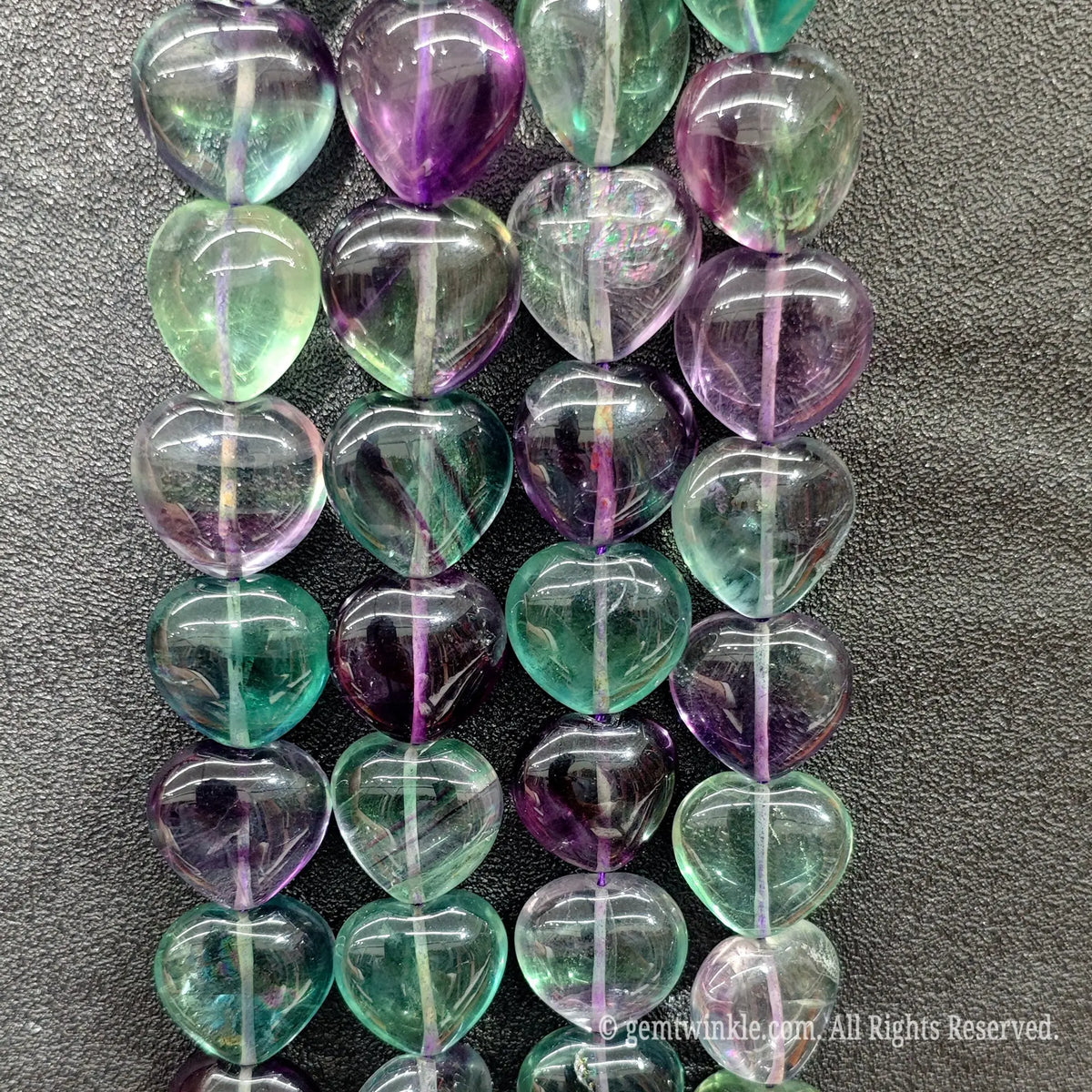 Close up view of natural rainbow fluorite heart beads showcasing polished glass like clarity and vibrant purple and green stripes