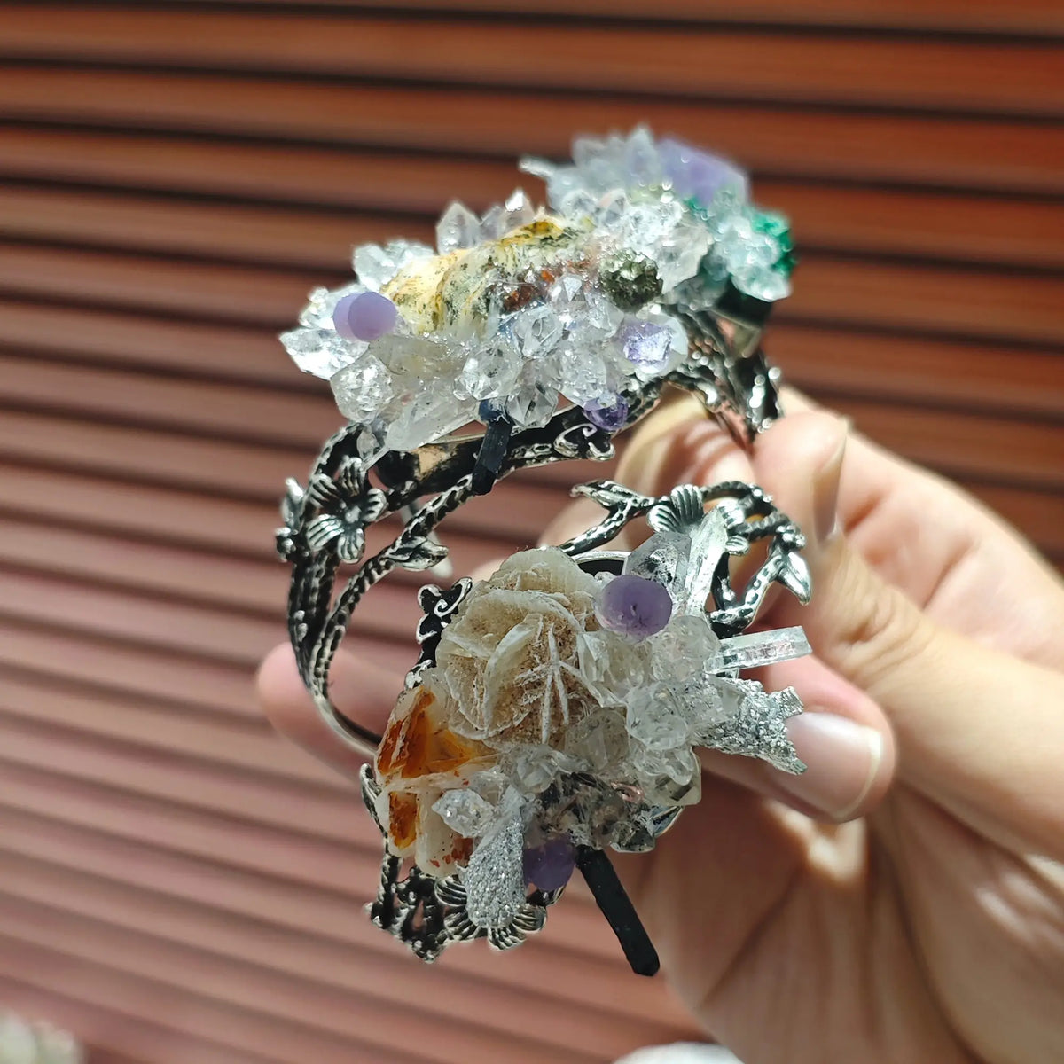 Hand displaying the raw unpolished crystal clusters and floral metal filigree on an adjustable cuff bracelet