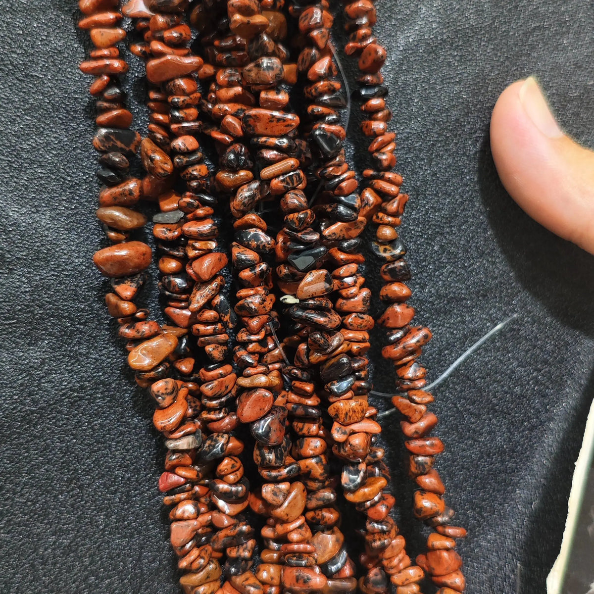 Fingers holding natural red eye obsidian gemstone chip beads on black background