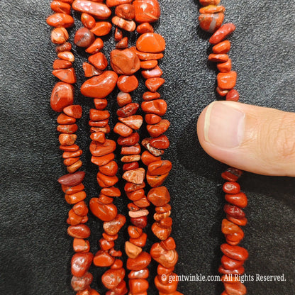 Close up hand holding natural red jasper stone chips displaying polished red surfaces and fine drill holes[cite: 10]