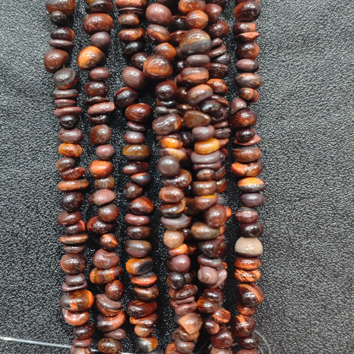 Close up of multi strands of red tiger eye 5-10mm irregular reddish brown chatoyant chips