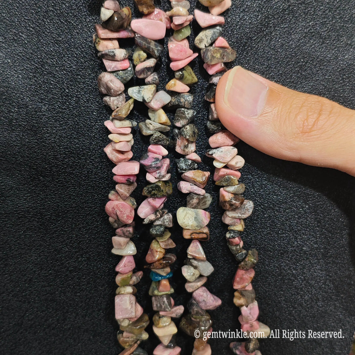 Close up hand holding natural rhodonite stone chips displaying polished vintage surfaces and fine drill holes[cite: 11]