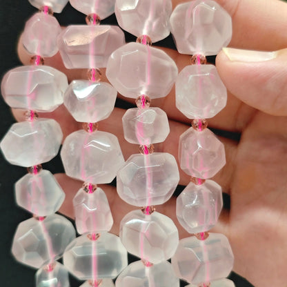 Hand displaying natural translucent rose quartz faceted freeform beads showing soft pink tones and pre-drilled center holes