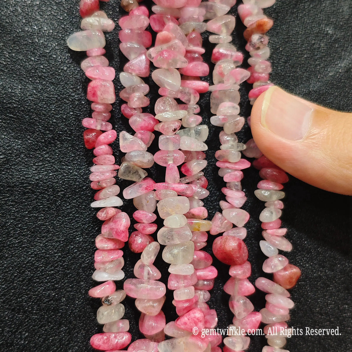 Close up hand holding natural cherry blossom agate stone chips displaying polished pink surfaces with fine drill holes
