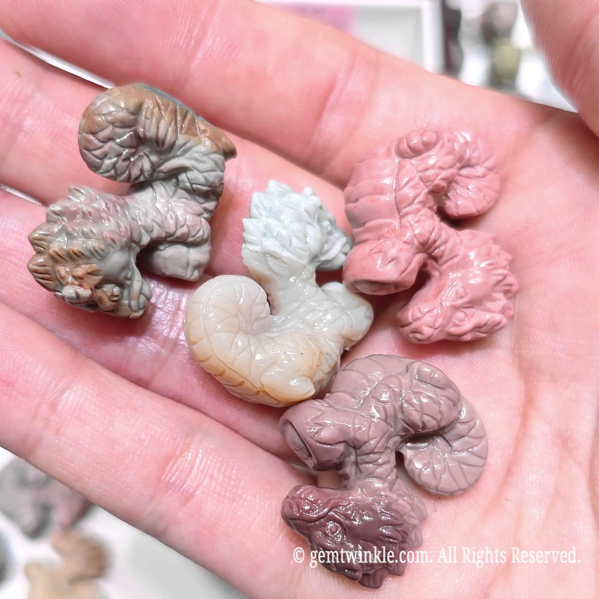 Close up view of natural Alxa agate dragon figurines holding money ingots resting on palm highlighting flat stable base