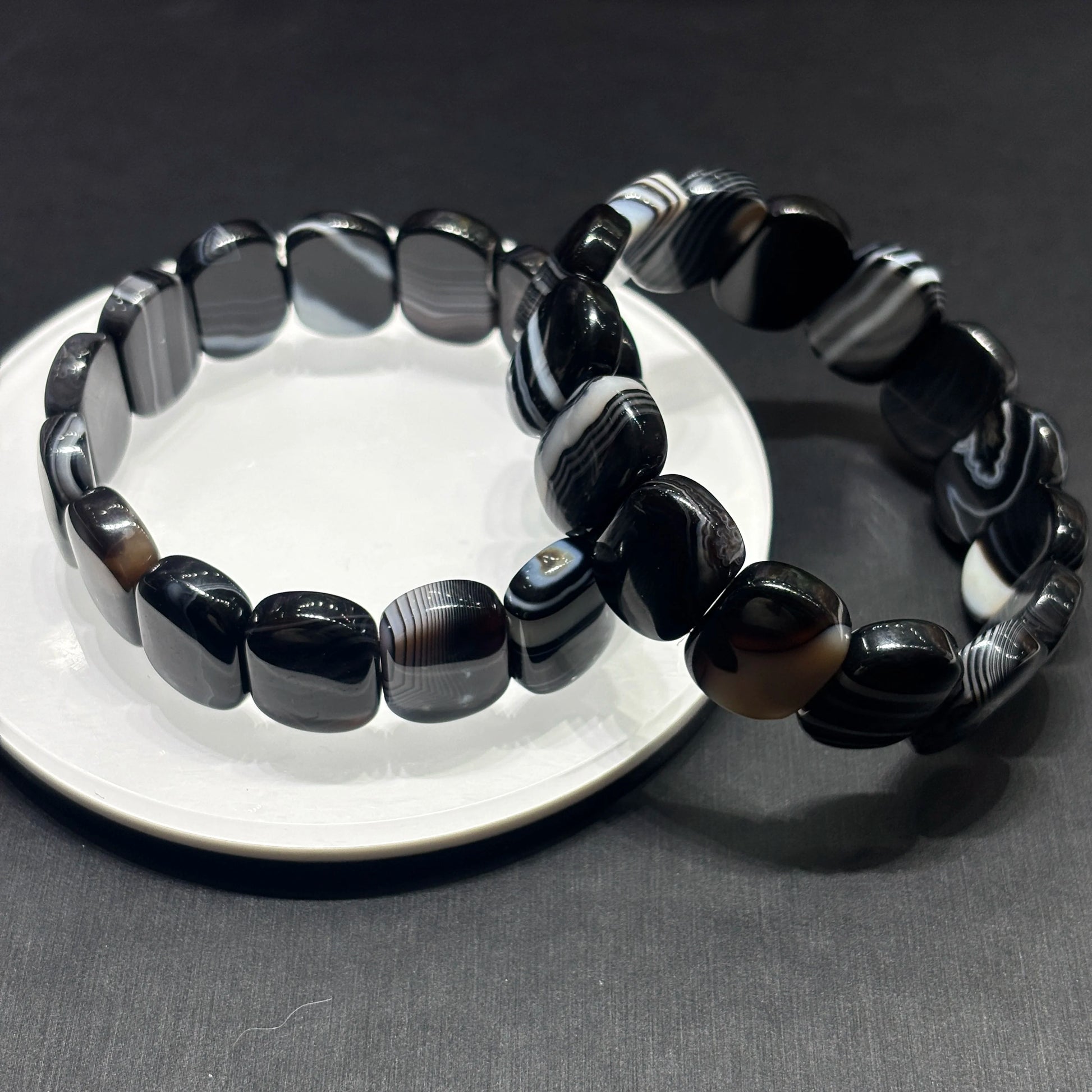 Two black and white banded onyx geometric square bracelets layered on white ceramic dish, contemporary aesthetic