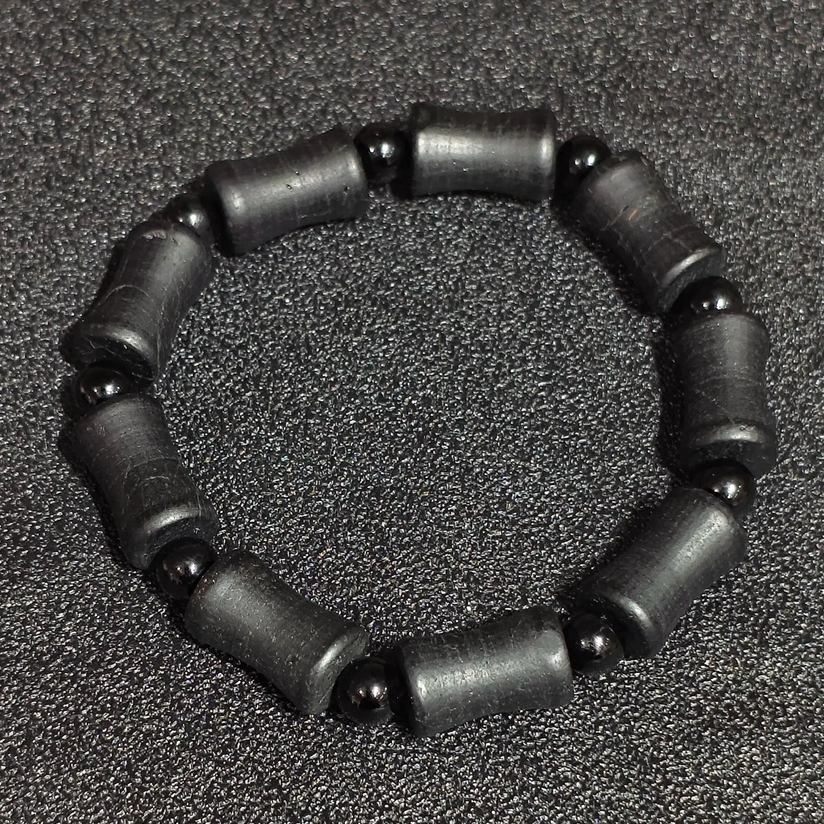 Natural matte black tourmaline barrel stretch bracelet displayed flat showing rustic cylinder beads and natural crystal striations