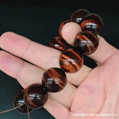 Side view emphasizing the three-dimensional curvature of the polished red tiger’s eye spheres as they sit on the wrist. No edges, no facets—pure round form.