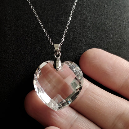 Side view of clear quartz heart pendant held in hand, emphasizing 3D depth, beveled edges, and silver bail connection