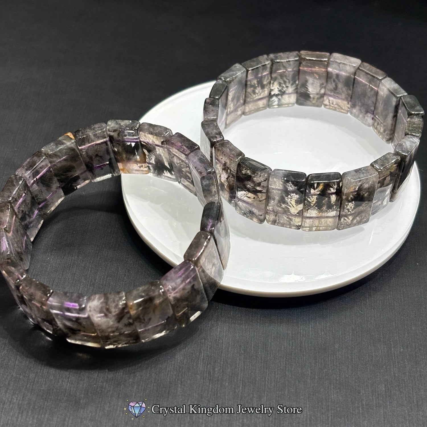 Black dream phantom quartz bracelet displayed on white ceramic disc, highlighting white dendritic inclusions and polished edges