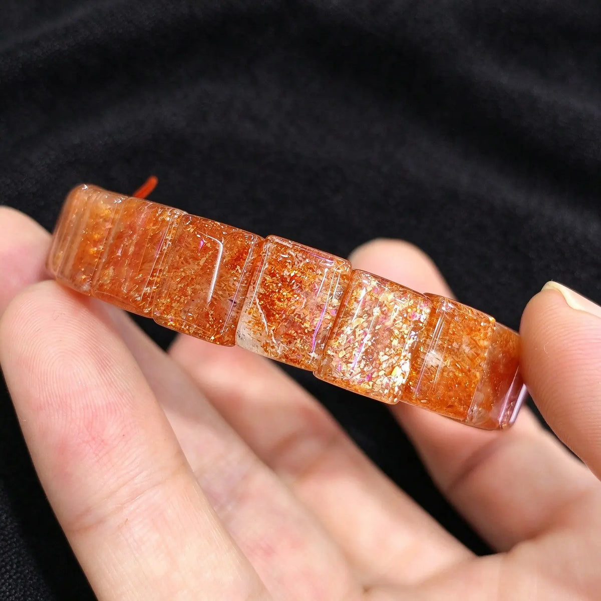 Hand holding a golden sunstone smooth block tile stretch bracelet highlighting metallic hematite flash under light