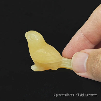 Side view of a honey yellow calcite cute bird statue showing its warm translucent color being held next to fingers for size comparison