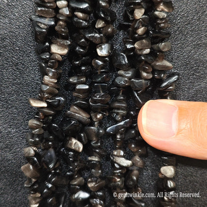 Fingers holding shimmering natural silver sheen obsidian gemstone chip beads on black background