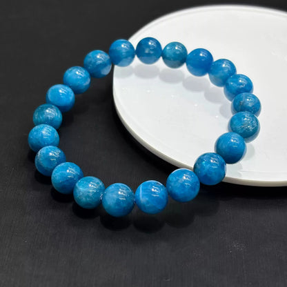 Blue apatite stretch bracelet arranged on white ceramic plate, showcasing vibrant sky-blue color and subtle internal crystalline patterns
